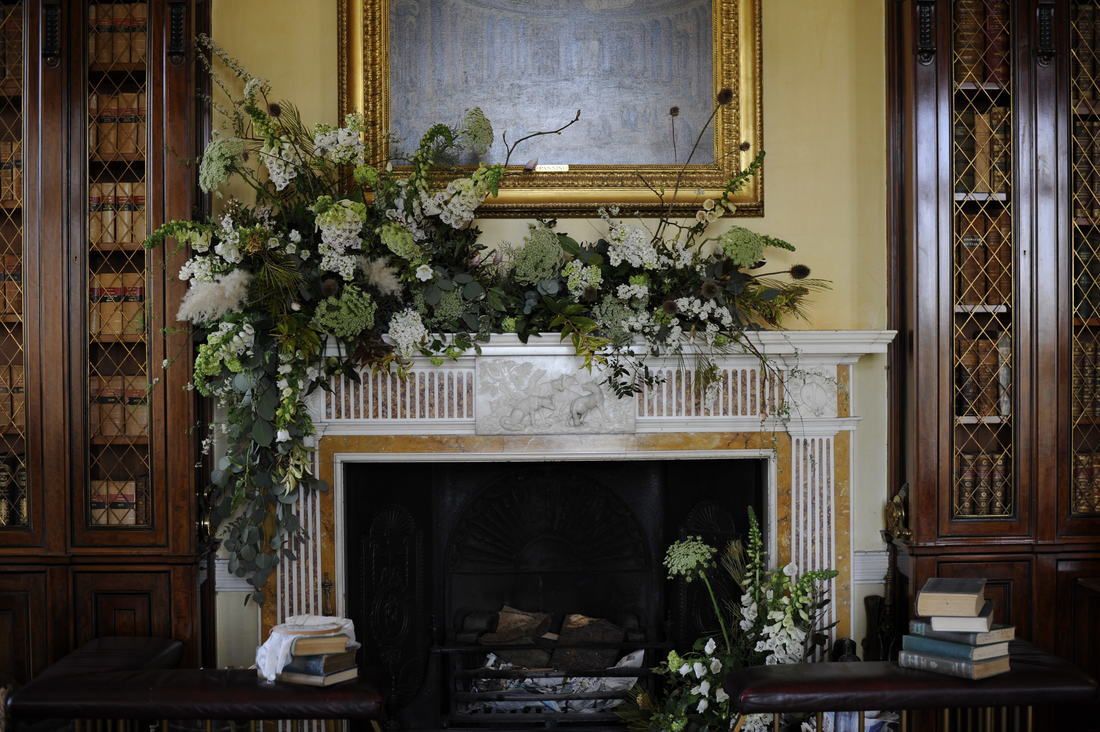 Elaborate spring floral arrangement of white and green tumbling over mantel and into fireplace