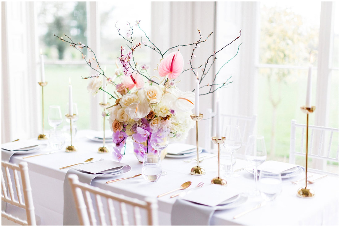 Table set with grey linen and gold cutlery. Pastel flowers in lilac, cream and pink