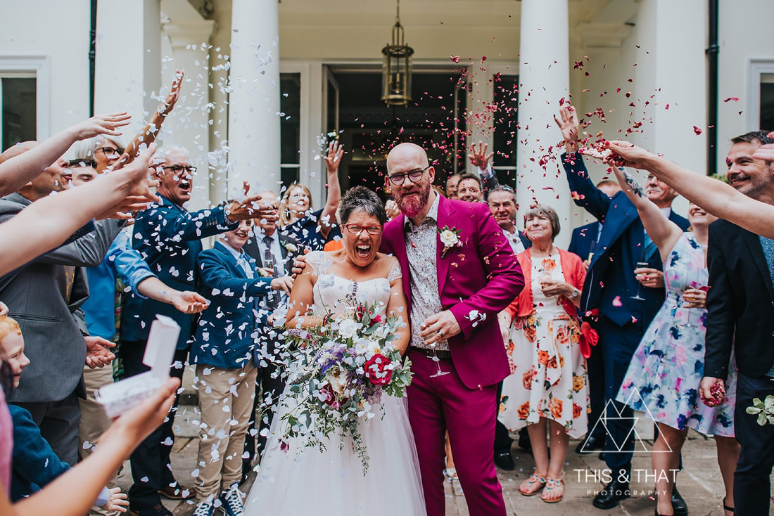 Confetti shot on portico of Penton Park. Bride in glasses and converse, groom in pink suit