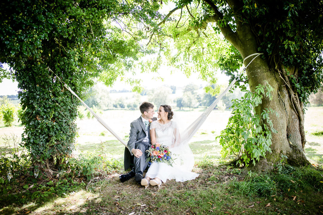 Bride and groom sit in a hammock in the grounds of exclusive country house venue Penton Park